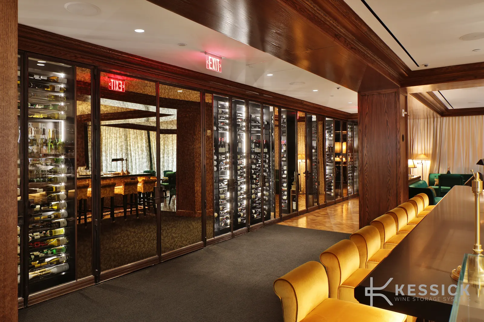 Hospitality lounge with glass-front wine storage walls along a bar lined with gold velvet seating