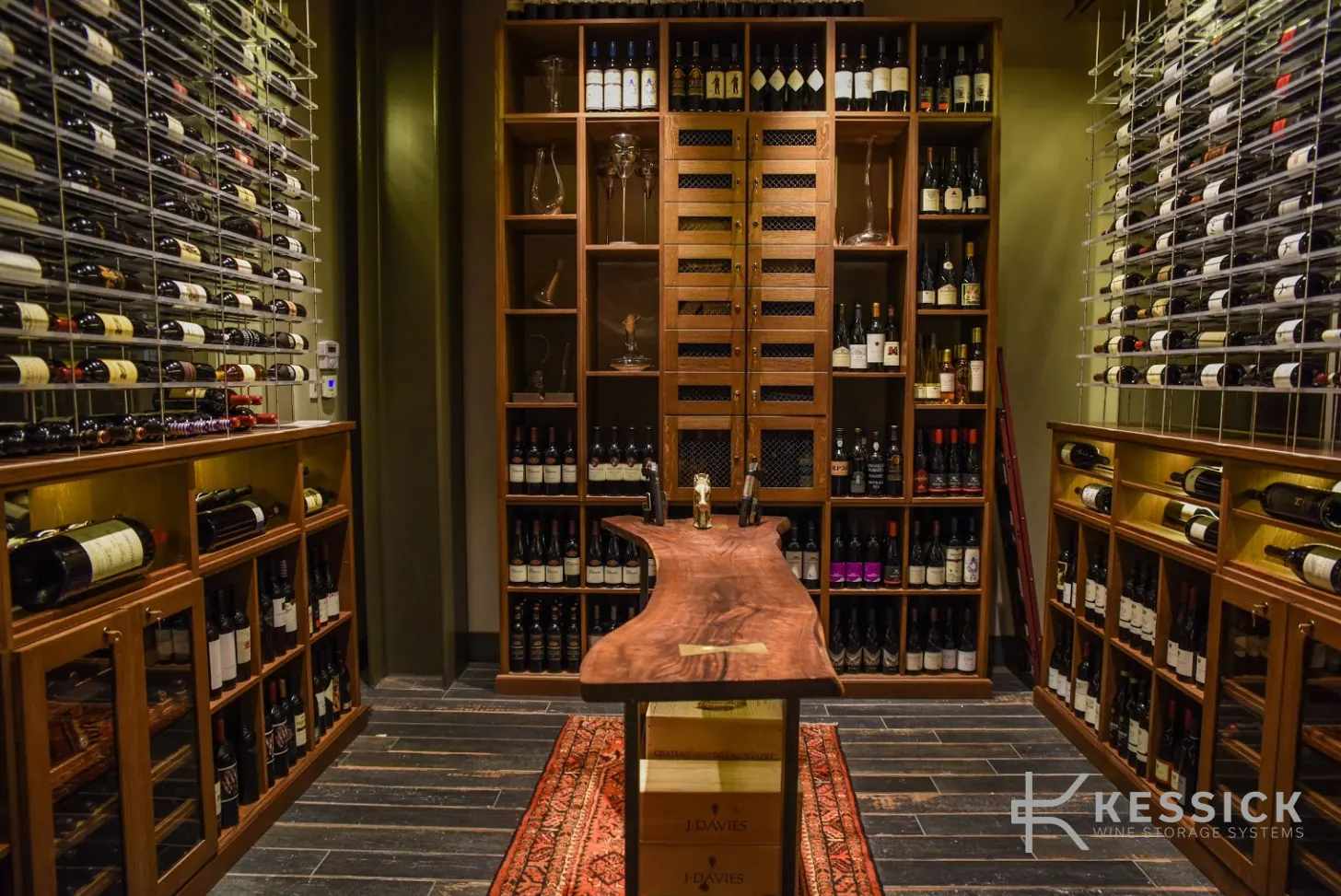 Wine storage room with labeled bottles organized on wood shelving and metal racks around a tasting table